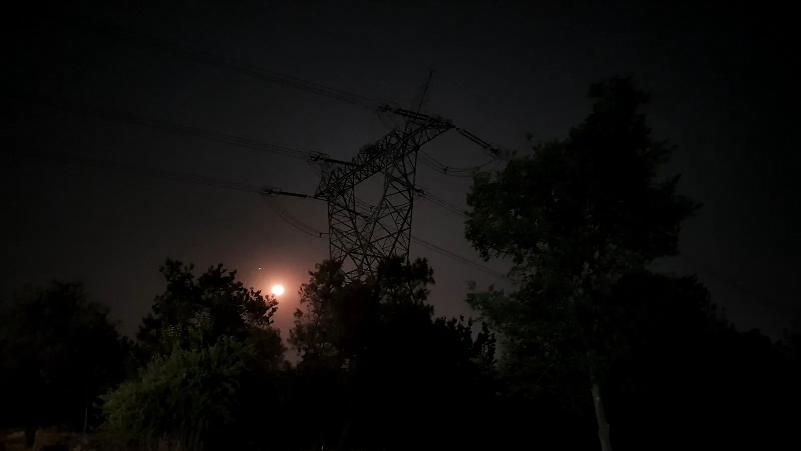 A high-voltage transmission pylon on the Gauteng Highveld at night, the moon and Venus low above the treeline.
